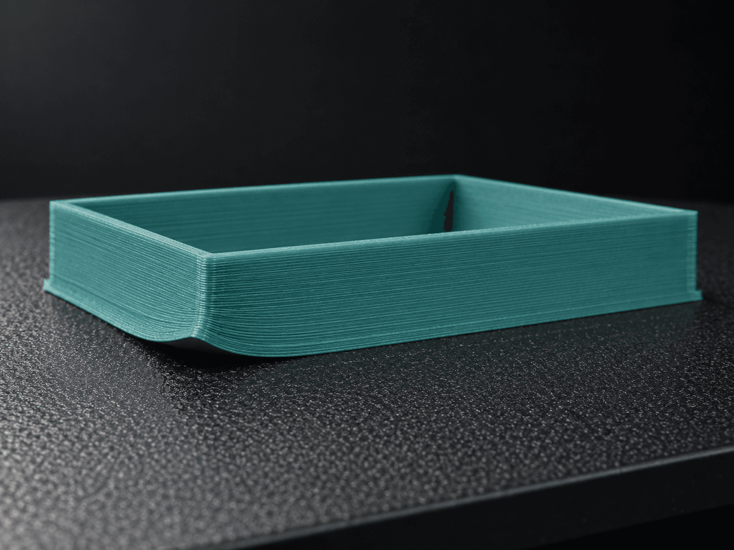 Illustration of a teal filament print with one corner lifting off the build plate